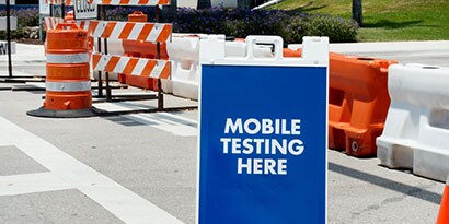 A temporary sign in front of temporary traffic control materials reads “Mobile testing here.
