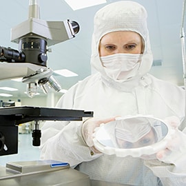 Suited lab technician examining semiconductor wafer in clean room with microscope