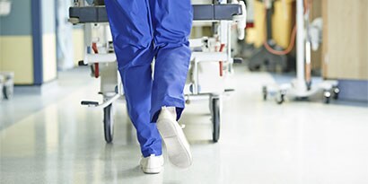 medical professional wheeling down a patient in a hospital hallway, with a focus on the hospital floor that is safe from hazards and cleaned with 3M floor care products.

