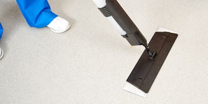 A uniformed health care worker cleans with the Easy Clean Disposable Floor Mop Pad in a commercial building.
