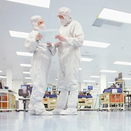 Two people in protective gear speaking in a lab.