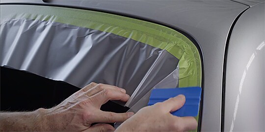 Video still with text “Wipe tape down with 3M Plastic Applicator PA-1” as being used on window edge
