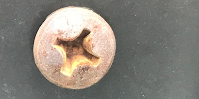 Pitting, rust, and galvanic corrosion detail on a metal screw head
