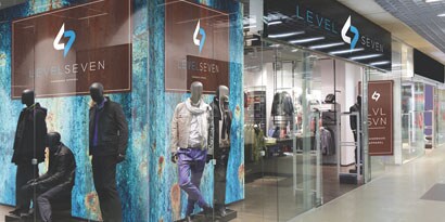 A shopping mall hallway features a wall wrap and overlaminate with images of models against a blue background.
