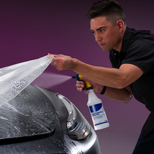 person spraying a plastic wrap on a car