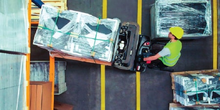 ภาพเหนือศีรษะของพนักงานบังคับรถยกขณะยกพาเลทข้ามช่องจราจรที่ติดเทปทำเครื่องหมายไว้
