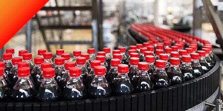 Hundreds of plastic bottles of dark soft drinks on a conveyer belt
