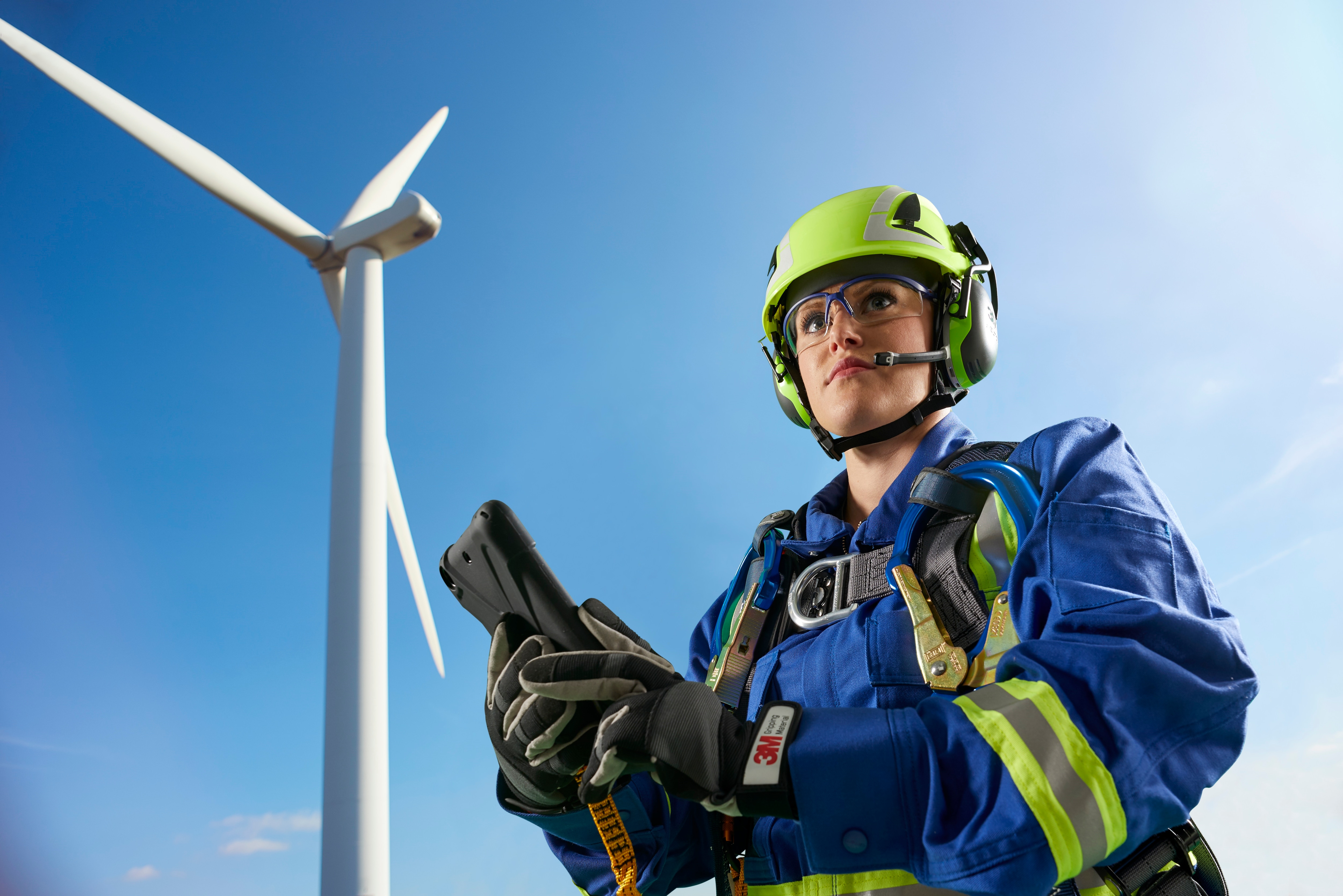 Energy and utilities worker standing in front of wind turbine wearing industrial safety PPE products