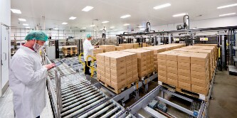 Image of masked workers in a clean white room keeping track of stacks of packages
