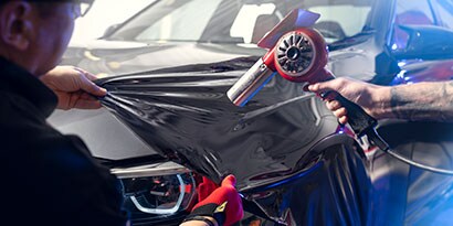 ตัวติดตั้งกราฟิกดึง Gloss Black 3M™ Wrap Film Series 2080 ไว้บนฝากระโปรงรถในขณะที่ตัวติดตั้งอื่นร้อน
