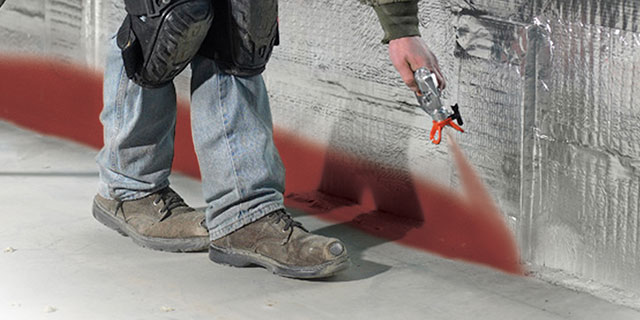 Worker spraying a firestop product along a wall-floor joint
