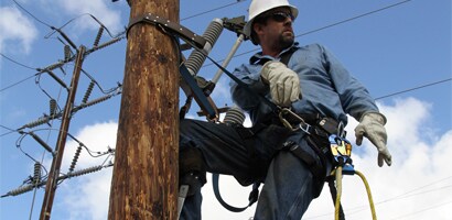 Workman on power pole wearing work positioning belt
