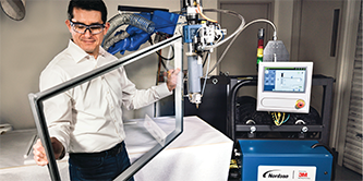 รูปภาพของชายคนหนึ่งกำลังถือกรอบซึ่งหุ่นยนต์ติดเทป 3M™ VHB™ Extrudable Tape อยู่ด้านหลัง
