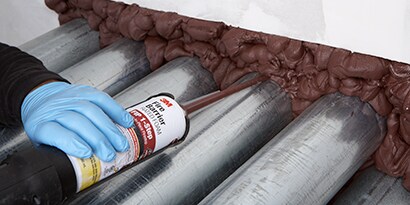 An installer applies 3M™ Fire Barrier Rated Foam FIP 1-Step around pipes in a through-penetration