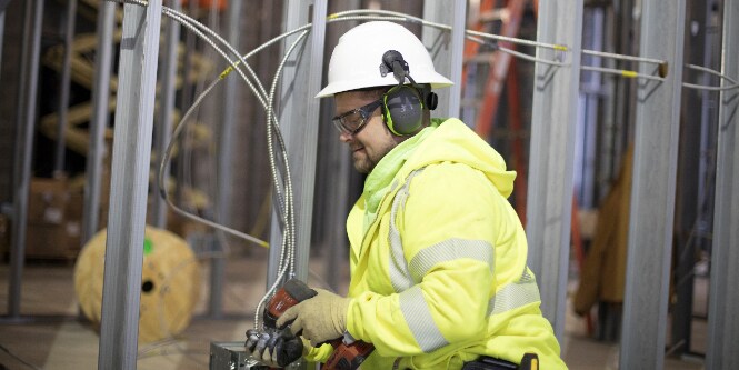 Image of a worker in protective gear on a construction site and carrying a cordless tool
