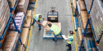 Overhead view of workers transferring cartons from a pallet to a shelf
