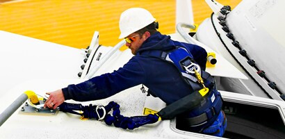 Worker reaching out of access port in wind turbine and fastening lanyard to anchor point
