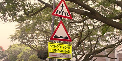 A traffic sign with fluorescent sign sheeting reads, “SCHOOL ZONE 220 m.”
