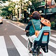 Adult riding bicycle with small child in child seat on urban road near crosswalk.
