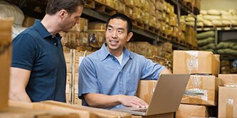 Image of two workers standing in a warehouse reviewing data on a laptop computer
