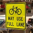 Yellow road sign with image of bicycle and words “may use full lane.”