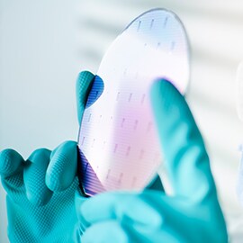 Two hands in lab gloves holding a wafer that used 3M's Wafer Support System for semiconductor manufacturing.