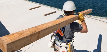 Worker at height carrying lumber while wearing fall protection PPE
